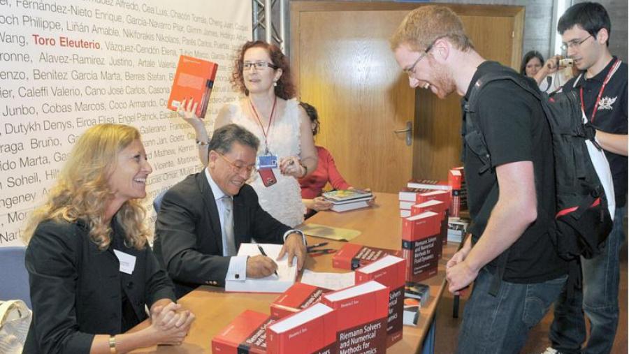 O profesor Eleuterio Toro, en presenza da profesora Vázquez Cendón (de pé detrás del), asina exemplares do seu manual